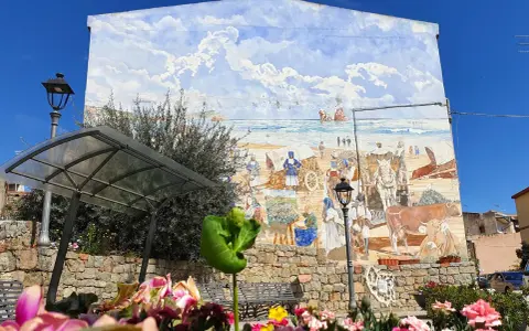 Un murale colorato a Loceri, Sardegna, raffigura scene di vita marina e rurale con persone, carri e animali sotto un cielo azzurro e nuvoloso.
