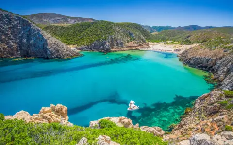 La splendida spiaggia di Buggerru, con acque cristalline e rocce imponenti, invita al relax. Una barca bianca solca il mare turchese.