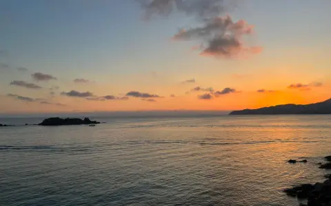 Un tramonto mozzafiato sul mare, con un'isola rocciosa e una barca a vela. Un luogo perfetto per ammirare dove vedere il tramonto a Villasimius.