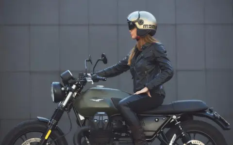 Donna in giacca di pelle e casco dorato, seduta su una moto verde. Non è chiaro dove si buttano i caschi da moto, ma questo è un ottimo esempio di come indossarli.