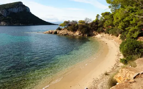 Spiaggia dorata e acque cristalline nella baia di Cala Moresca, con una scogliera verdeggiante e un promontorio roccioso sullo sfondo.