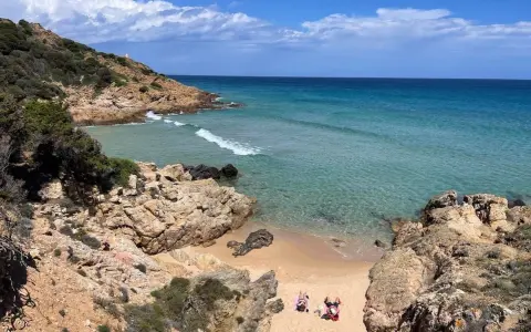 Spiaggia selvaggia vicino al centro storico di Chia, con rocce dorate, mare cristallino e due persone che prendono il sole.