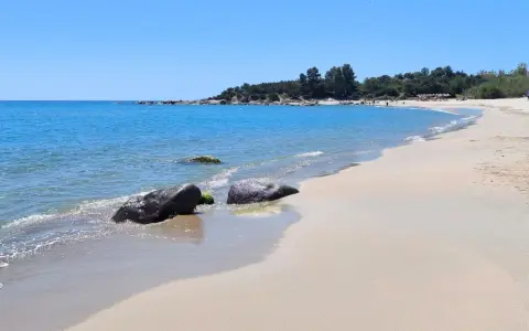 Spiaggia di Lido di Orrì con rocce scure bagnate dall'acqua cristallina e sabbia dorata.