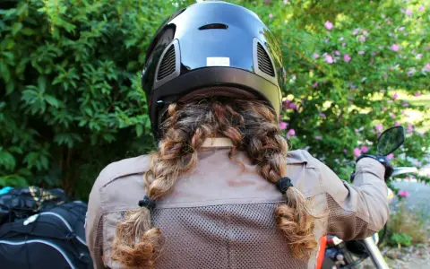 Donna con casco nero e capelli raccolti in due trecce, pronta per legare il casco alla moto.