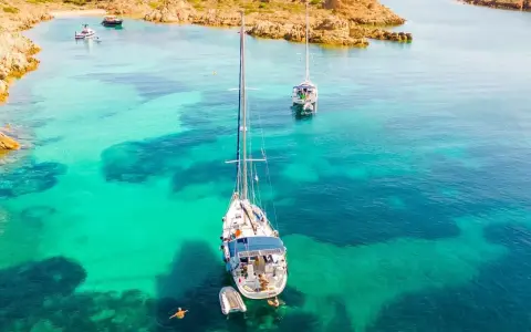 Vela al largo di Cala Ambra, con acque cristalline e un paesaggio roccioso.