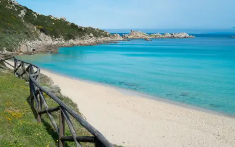 Una splendida spiaggia rena bianca bagnata da un mare cristallino. La vegetazione mediterranea e le rocce scolpite dal vento completano il paesaggio.