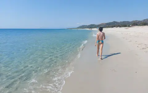 Bambino cammina su una delle splendide spiagge della costa est della Sardegna, con mare cristallino e sabbia bianca.
