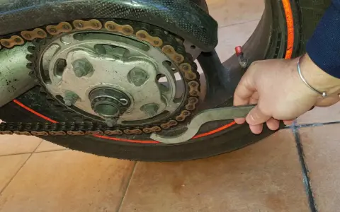 Mano con chiave inglese che lavora sulla catena di una moto, mostrando come tirare la catena della moto per la manutenzione.