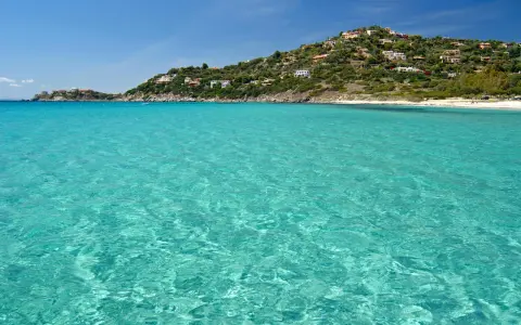 Acque cristalline e una collina verdeggiante punteggiata di case bianche e rosse, con la **spiaggia Torre delle Stelle** che si estende in lontananza.