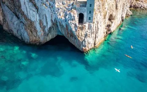 Porto Flavia, un'antica struttura legata alle miniere abbandonate della Sardegna, si affaccia su un mare cristallino. Kayak solcano le acque turchesi.