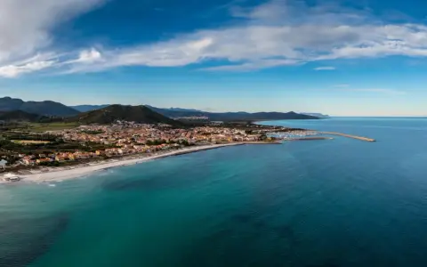Vista aerea di Posada, Siniscola, con la sua spiaggia dorata, il mare turchese e le case colorate che si affacciano sulla costa.
