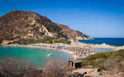 Una giornata di sole a Punta Molentis beach, con acque cristalline, sabbia dorata e tante persone che si godono il mare.