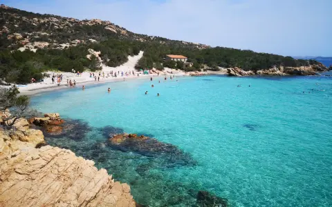 La **cala Granara** splende con acque cristalline e una spiaggia affollata di bagnanti. Rocce dorate emergono dal mare turchese.