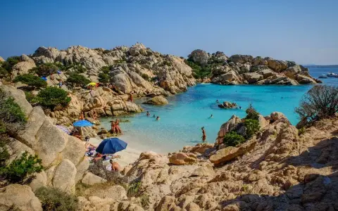 Una baia con rocce granitiche scolpite dal vento e acque turchesi cristalline, tra le spiagge più belle sardegna nord. Gente rilassata sotto gli ombrelloni.