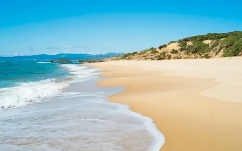 Onda bianca accarezza la sabbia dorata della spiaggia di Scivu, sotto un cielo azzurro intenso.