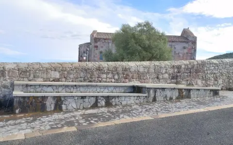 Fontana in pietra con scorci di un antico edificio religioso, un'oasi di pace ad **Allai, Sardegna**.