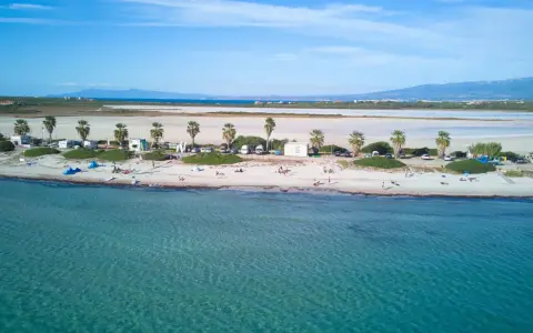 Spiaggia di Putzu Idu con palme, camper e gente che si gode il sole. Acqua cristallina e cielo azzurro.