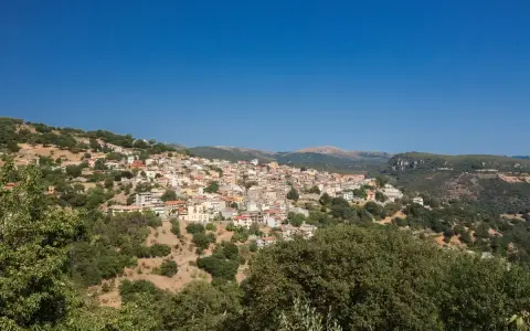 Panoramica di Seulo, Sardegna, con case colorate arroccate su una collina verdeggiante sotto un cielo azzurro.