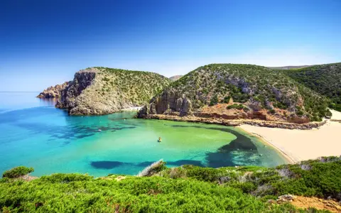 Baia con acque cristalline e sabbia dorata, incastonata tra scogliere verdi. Un vero gioiello tra le spiagge più belle in Sardegna.