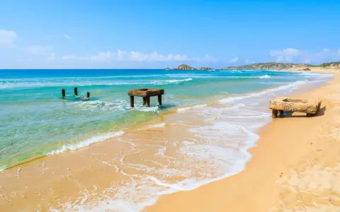 Spiaggia di Chia, Cagliari. Resti di antiche strutture in mare e sulla sabbia dorata, con acque turchesi e cielo azzurro.