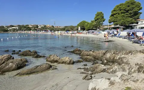 Spiaggia del Pellicano: sabbia chiara, rocce levigate e mare cristallino con bagnanti e ombrelloni.