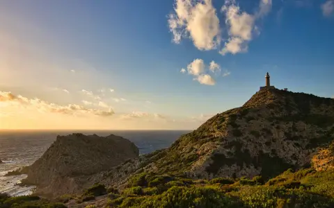 Faro solitario su una collina rocciosa, con il mare e le nuvole al tramonto. Un paesaggio mozzafiato di Nebida, Sardegna.