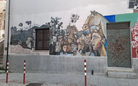 Un grande murale colorato decora un edificio in un paese, con volti, un cavallo e bandiere. Un'opera d'arte che racconta storie di un paese, murales in Sardegna.