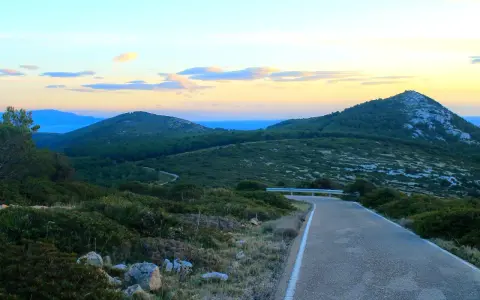 Strada panoramica verso il monte Doglia al tramonto, con colline verdi e cielo colorato.