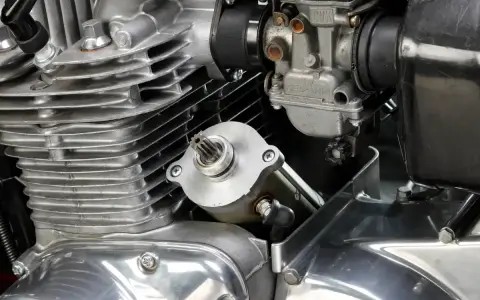 Dettaglio del motore di una moto: il test del motorino di avviamento è in primo piano, con il carburatore e le alette di raffreddamento visibili.