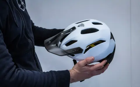 Mani che tengono la calotta esterna di un casco da bici bianco con visiera scura e logo Dainese.
