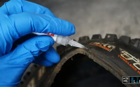 Mano con guanto blu applica colla per pneumatici tubeless riparazione su un copertone da MTB.