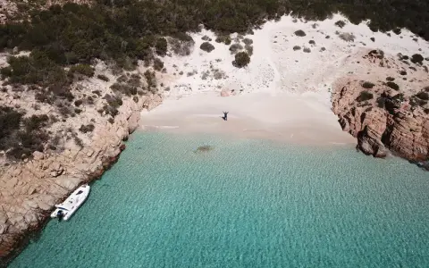 Una persona celebra la bellezza di Cala Soraya, con acque cristalline e rocce rosse. Una barca è ormeggiata.