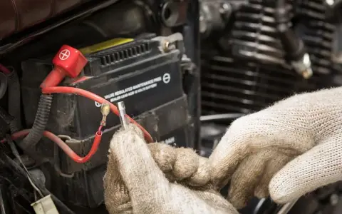 Mani guantate lavorano sulla batteria 12V della moto, forse per il tempo di ricarica.
