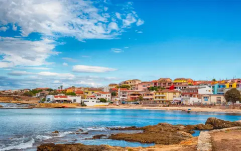 Colorate case affacciate sul mare blu, con rocce in primo piano. Il centro storico di Porto Torres, un incanto sardo.