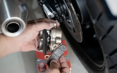 Mani che sostituiscono pastiglie cristallizzate su una moto. Si vede la pinza del freno e il disco.