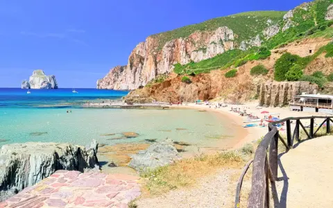 Spiaggia di Masua con acque cristalline, scogliere imponenti e il Pan di Zucchero all'orizzonte. Relax e natura incontaminata.