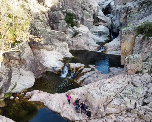 Un gruppo di escursionisti ammira un canyon con cascate e pozze d'acqua cristallina. Uno di loro, con un giubbotto rosa acceso, sembra dire "bau mela!" alla natura.