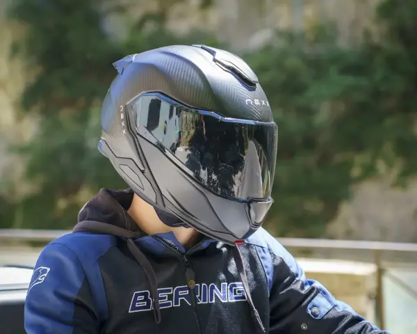 Casco da moto nero con visiera riflettente, che offre una sensazione di pressione sulla fronte. Indossato da una persona con giacca blu e nera.