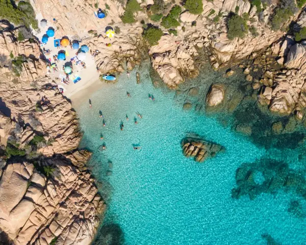 Vista aerea della spiaggia di Cala Coticcio, con bagnanti che si godono le acque cristalline e ombrelloni colorati sulla sabbia dorata.