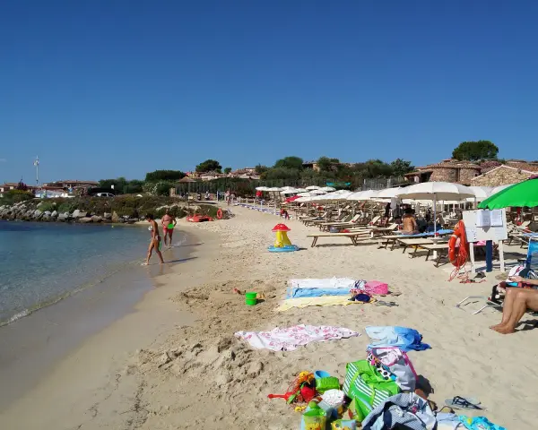 A sunny beach with people walking in the shallow water and lounging under umbrellas.