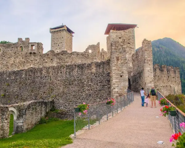Un sentiero fiorito conduce al maestoso Castello San Michele, con le sue torri imponenti e mura antiche che si stagliano contro il cielo.