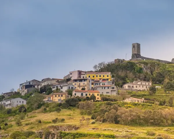 Il castello di Osilo domina un borgo colorato su una collina verdeggiante, sotto un cielo azzurro.