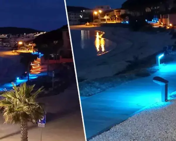 Passeggiata illuminata da luci blu sul lungomare di Golfo Aranci sera, con palme e case sullo sfondo.