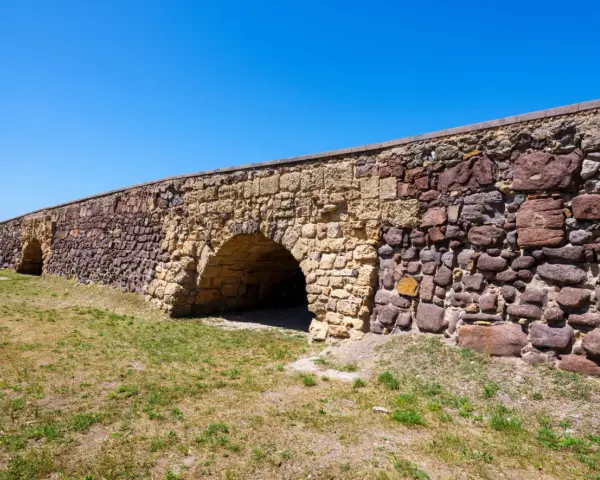 Antico ponte romano a Sant'Antioco, con archi in pietra e un muro imponente sotto un cielo azzurro.