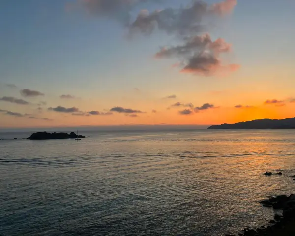 Un tramonto mozzafiato sul mare, con un'isola rocciosa e una barca a vela. Un luogo perfetto per ammirare dove vedere il tramonto a Villasimius.