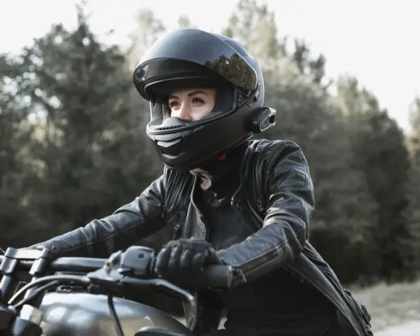 Woman in black leather jacket and helmet riding a motorcycle outdoors.