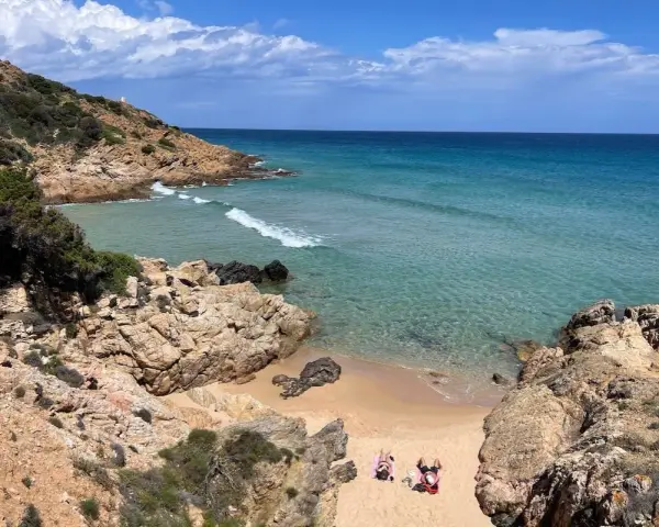 Spiaggia selvaggia vicino al centro storico di Chia, con rocce dorate, mare cristallino e due persone che prendono il sole.