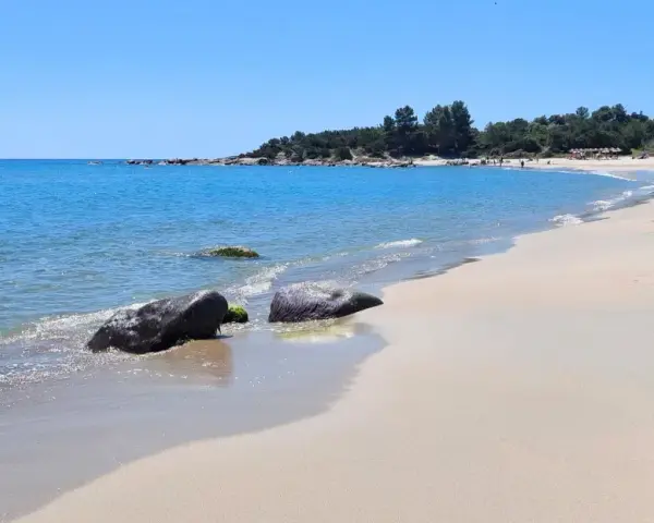 Spiaggia di Lido di Orrì con rocce scure bagnate dall'acqua cristallina e sabbia dorata.