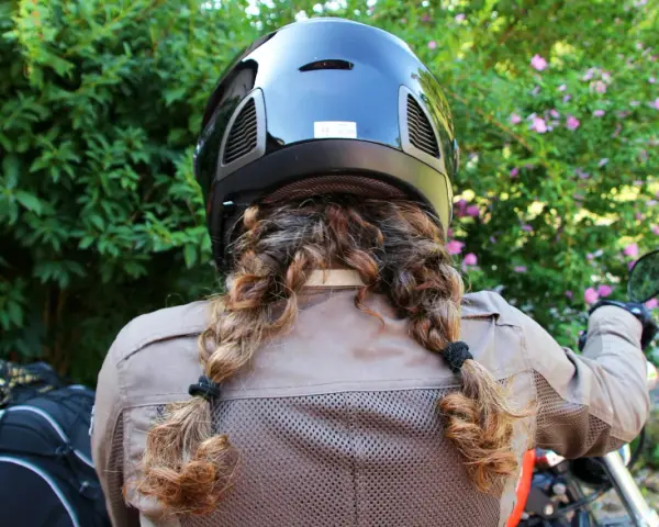Donna con casco nero e capelli raccolti in due trecce, pronta per legare il casco alla moto.