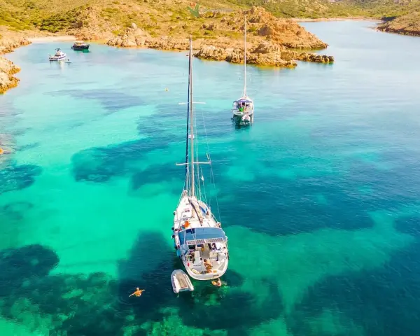 Vela al largo di Cala Ambra, con acque cristalline e un paesaggio roccioso.